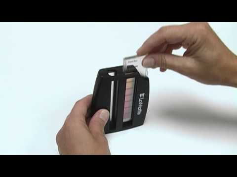 A person slides a test strip into a black handheld device with a color chart, likely using the High Range Molybdate Test Kit - 3346-01 to analyze water quality or chemical levels.