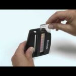 A person holds a Nitrate Nitrite Test Kit - 3519-01 with one hand and inserts a small test strip into it with the other, aligning the strip with the color chart on the device.